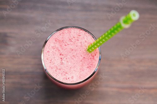 A top view of a watermelon smoothie in a glass with tube on a wooden background