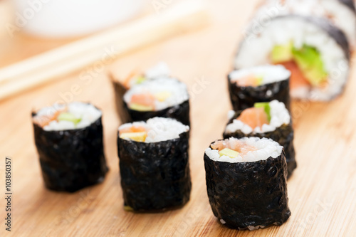 Sushi rolls with salmon, avocado, rice in seaweed and chopsticks