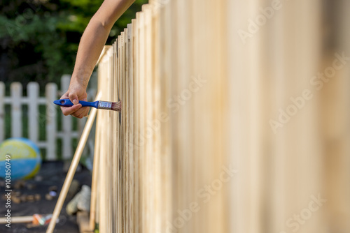 Female hand varnishing a wooden fence