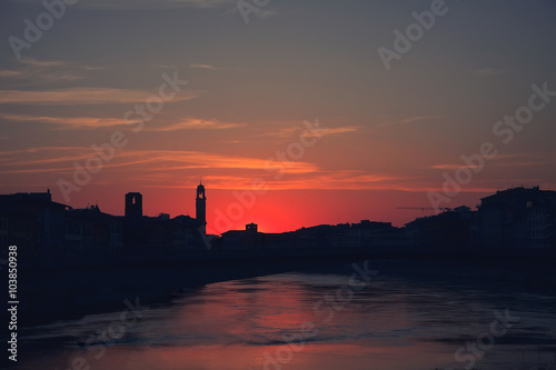 Sunset over black silhouette of Pisa cityline and Aron river 