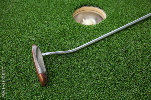 Putting golf club on green grass with golf ball in the hole 