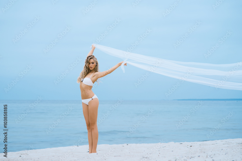 Beautiful blond with hot legs posing with a blowing silk on the beach.