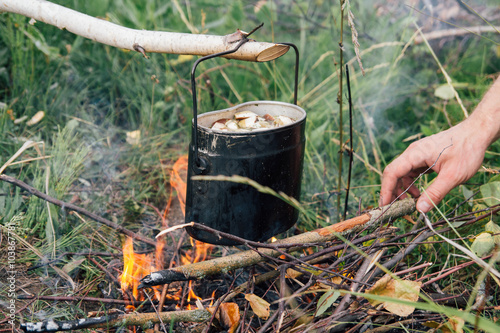 Iron pot cooks soup over open fire in a campsite
