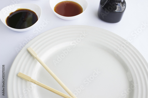 Plato blanco con palillos chinos acompañado de salsa de anguila y de soya photo