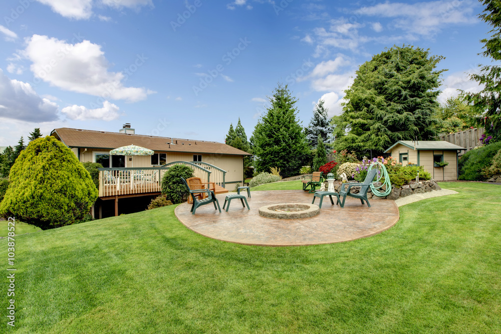 Fototapeta premium Large back yard with grass, circular patio, chairs, and garden.
