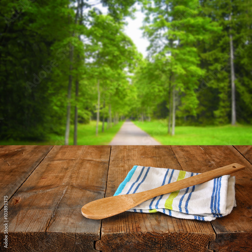 Kitchen utensils on tablecloth on wooden textures table against autumnal forest background 