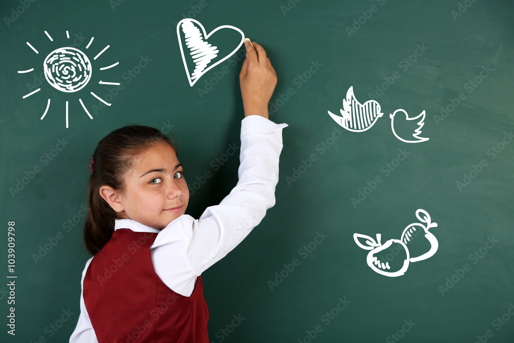 Beautiful little girl drawing on blackboard in classroom