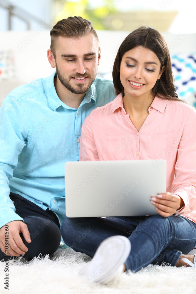 Happy couple sitting on the floor and working on laptop in a room Happy couple sitting on the floor and working on laptop in a room
