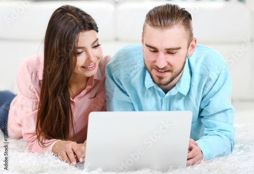 Happy couple lying on the floor and working on laptop