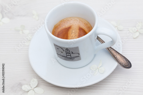 A cup of hot strong espresso on a white wooden table decorated with white hydrangea flowers