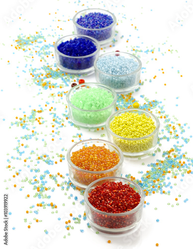 Row of glass bowls full of multicolored beads on white background