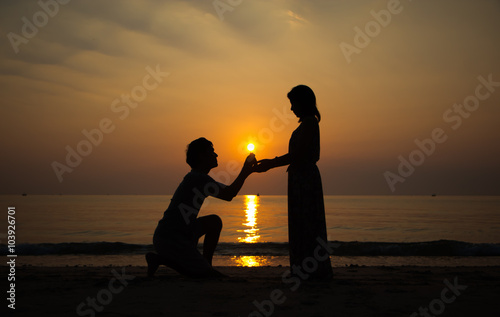 A backlit man propose marriage to a backlit woman with sunrise background