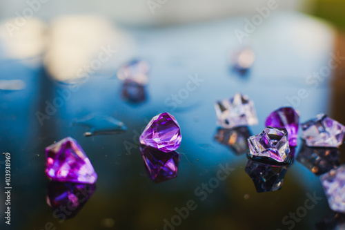 Diamond  small purple jewel  stones heap over mirror glass table  crystal stones  shiny gold and silver jewelery on a table
