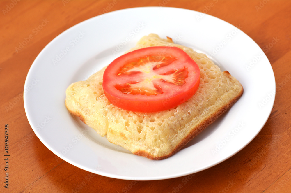 Square shape buttered English crumpet with slice of tomato