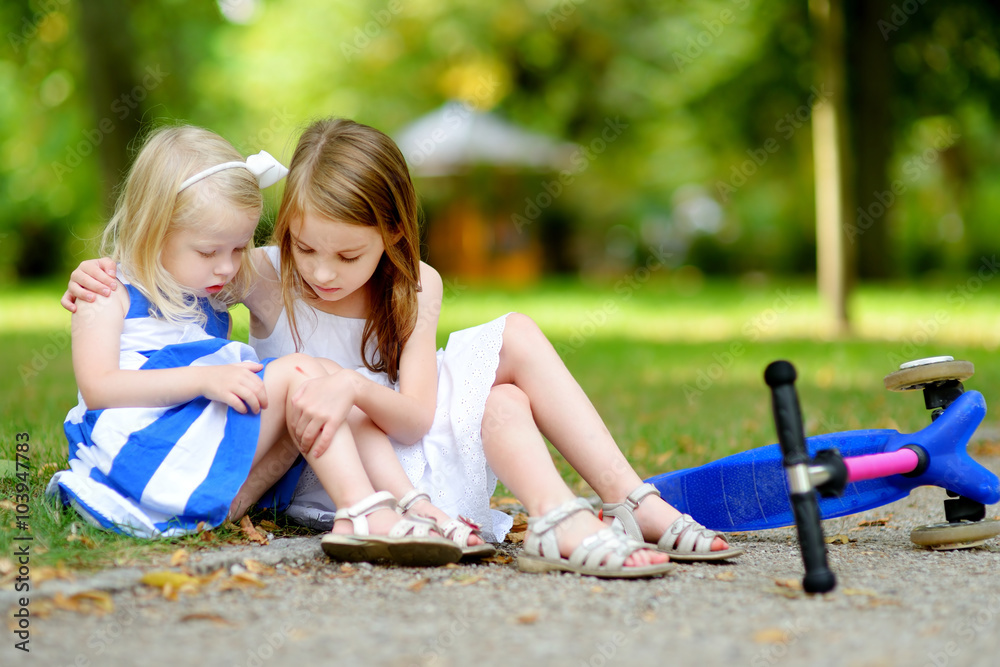 Little girl comforting her sister after she fell while riding her scooter Little girl comforting her sister after she fell while riding her scooter