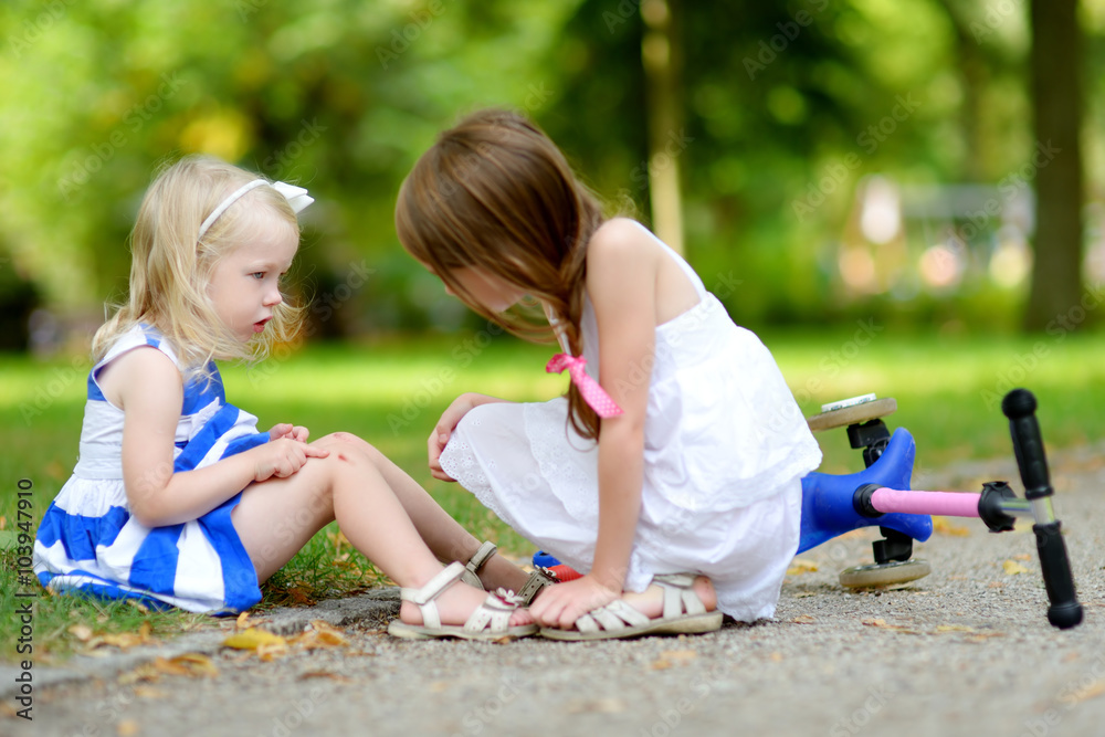 Little girl comforting her sister after she fell while riding her scooter Little girl comforting her sister after she fell while riding her scooter