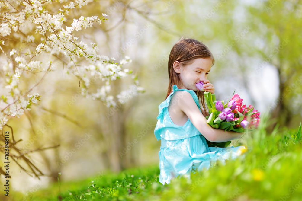 Adorable little girl holding tulips for her mother in blooming cherry garden Adorable little girl holding tulips for her mother in blooming cherry garden