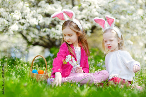 Two adorable little sisters hunting for easter egg in blooming spring garden