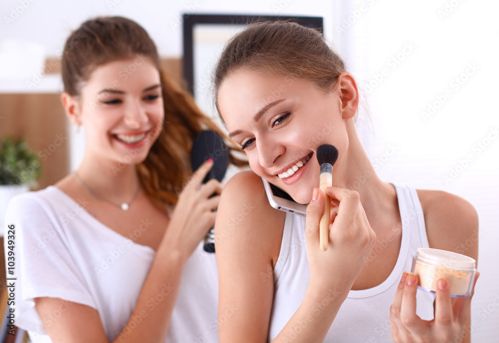 Beautiful girls looking in the mirror and applying cosmetic with a big brush Beautiful girls looking in the mirror and applying cosmetic with a big brush