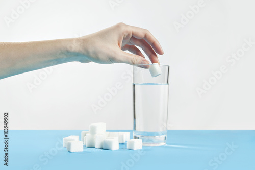 Glass of water against sugar, diabetes disease, sweet addiction, hand drop a sugar