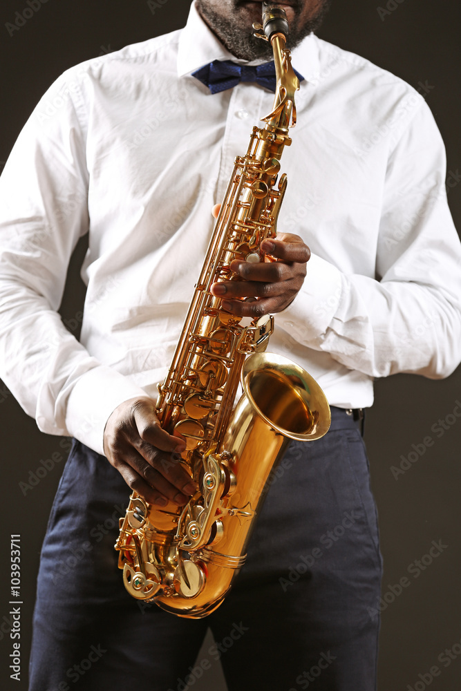 Fototapeta premium African american man playing golden brass saxophone with blue bow tie and white shirt, jazz music performance