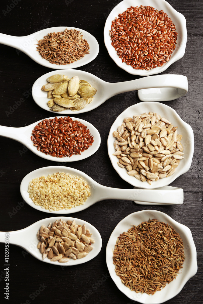 Different kinds of seeds in spoons on wooden table