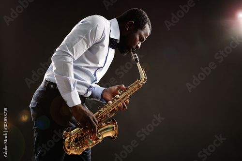 African American jazz musician playing the saxophone on grey background photo