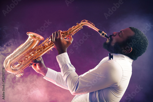 Photography African American jazz musician playing the saxophone against colorful smoky back