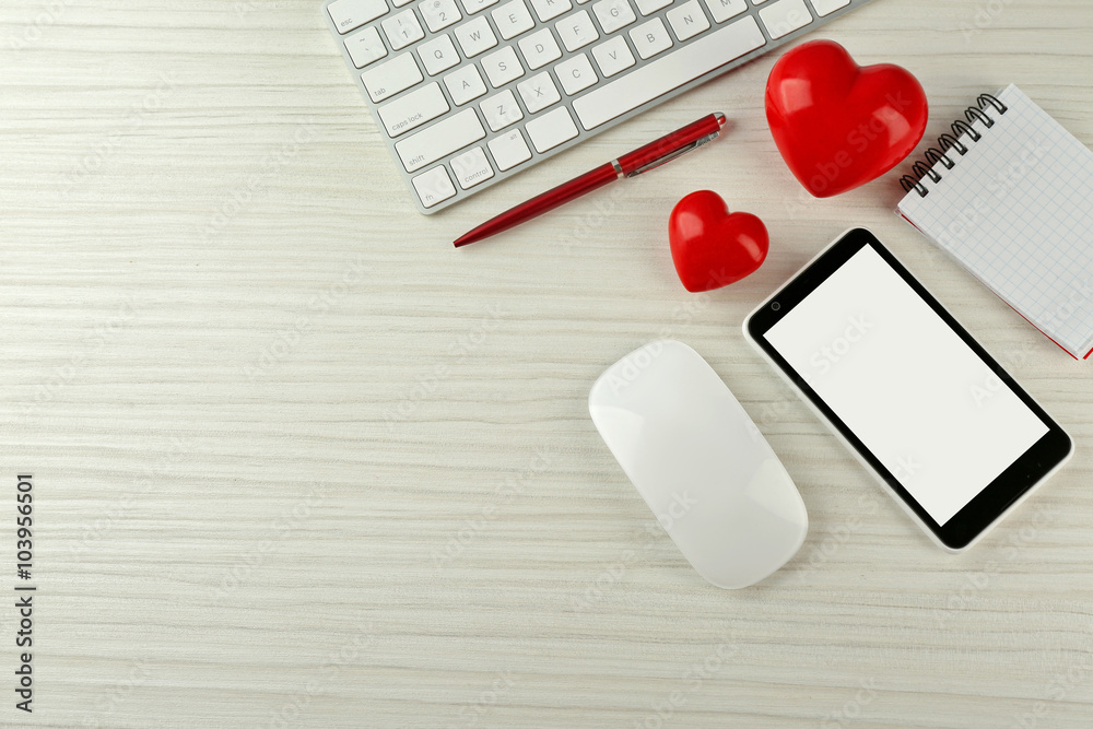 Computer peripherals with red hearts, notebook and mobile phone on light wooden table Computer peripherals with red hearts, notebook and mobile phone on light wooden table
