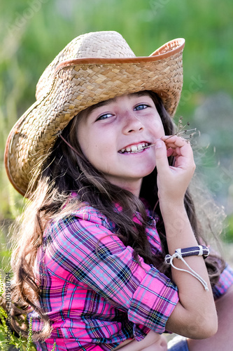 little girl sitting in a field wearing a cowboy hat