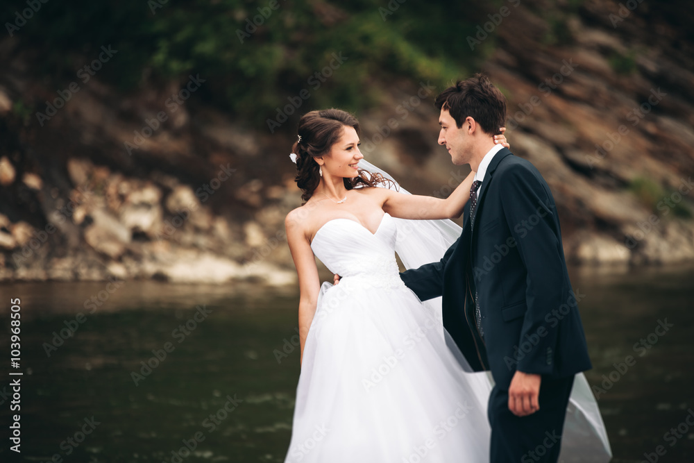 Naklejka premium Beautifull wedding couple kissing and embracing near the shore of a mountain river with stones 