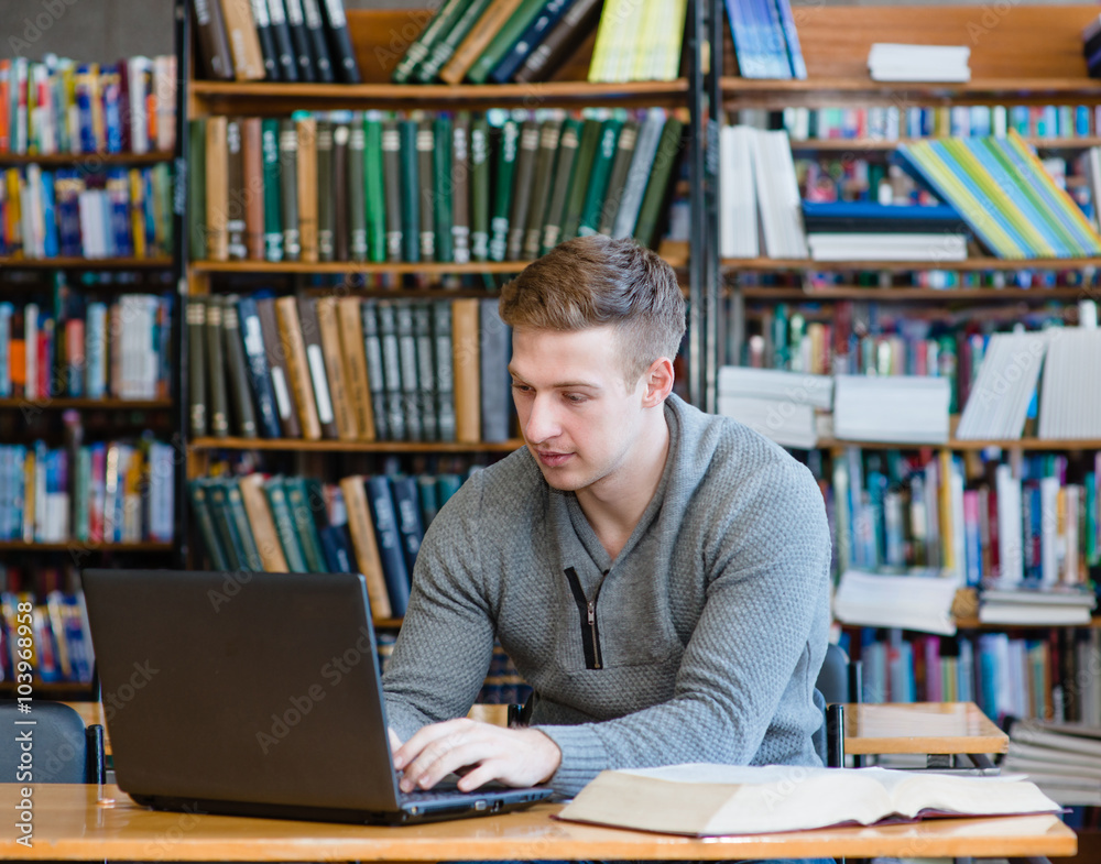 Young male student using laptop in the university library Young male student using laptop in the university library