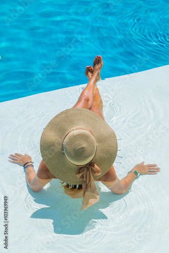 Woman sitting in a swimming pool in a sunhat
