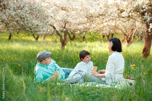 Young family picnicking in blooming apple garden