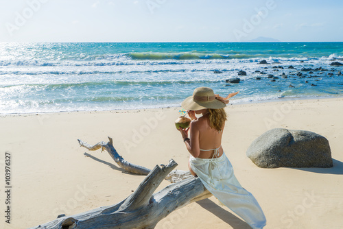 Woman sitting on a tree trunk at the tropical beach holding a fr