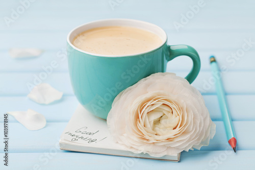 Fotografija Coffee cup with spring flower and notes good morning on blue rustic background,
