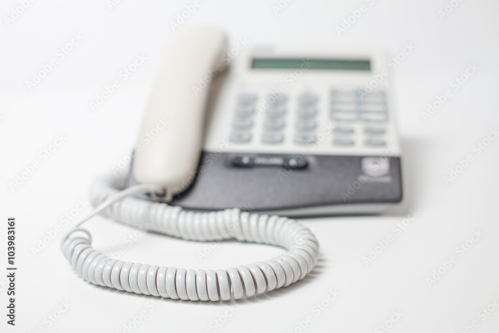 White digital phone with handset and cord on white table White digital phone with handset and cord on white table