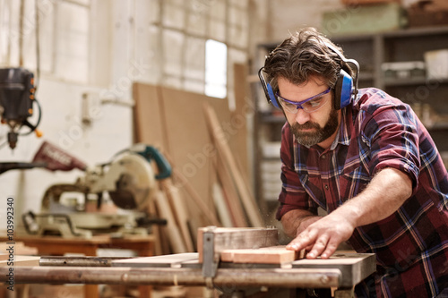 Carpenter working with machinery cutting a wooden plank