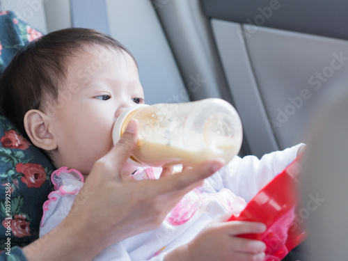 Asian toddler eating bottle of milk and sitting in car while tra photo