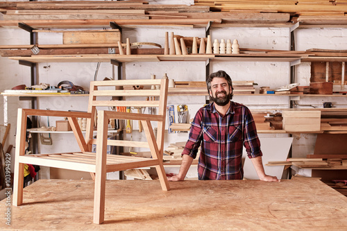 Smiling craftsman in his woodwork studio with wooden chair frame
