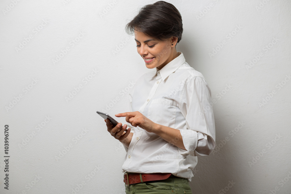 Attractive young woman standing against a wall texting on her smartphone Attractive young woman standing against a wall texting on her smartphone