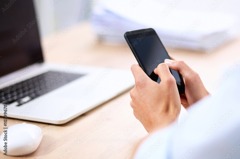 Businesswoman sending message with smartphone sitting in the office