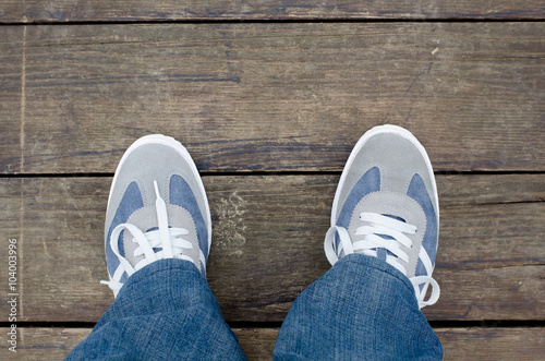 Sport shoes and legs in jeans from above on wooden dock floor