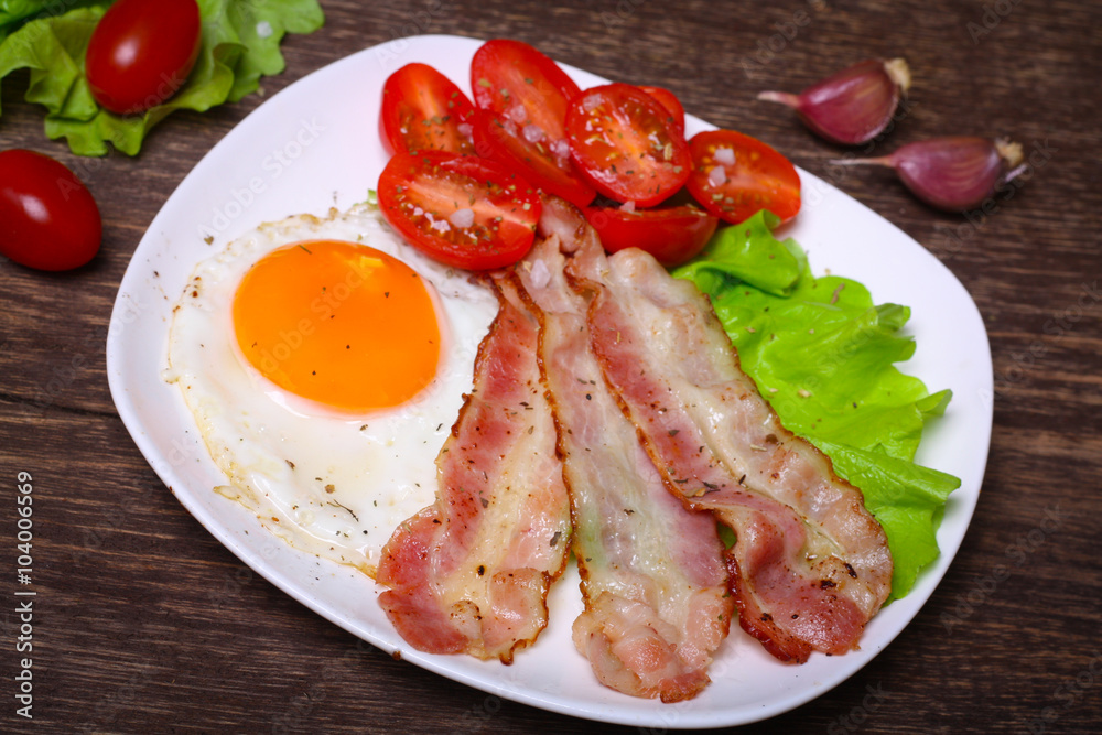 Hearty breakfast. Fried egg with bacon and tomatoes on a wooden background Hearty breakfast. Fried egg with bacon and tomatoes on a wooden background