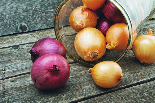 Yellow and red onions in a glass jar on a wooden background