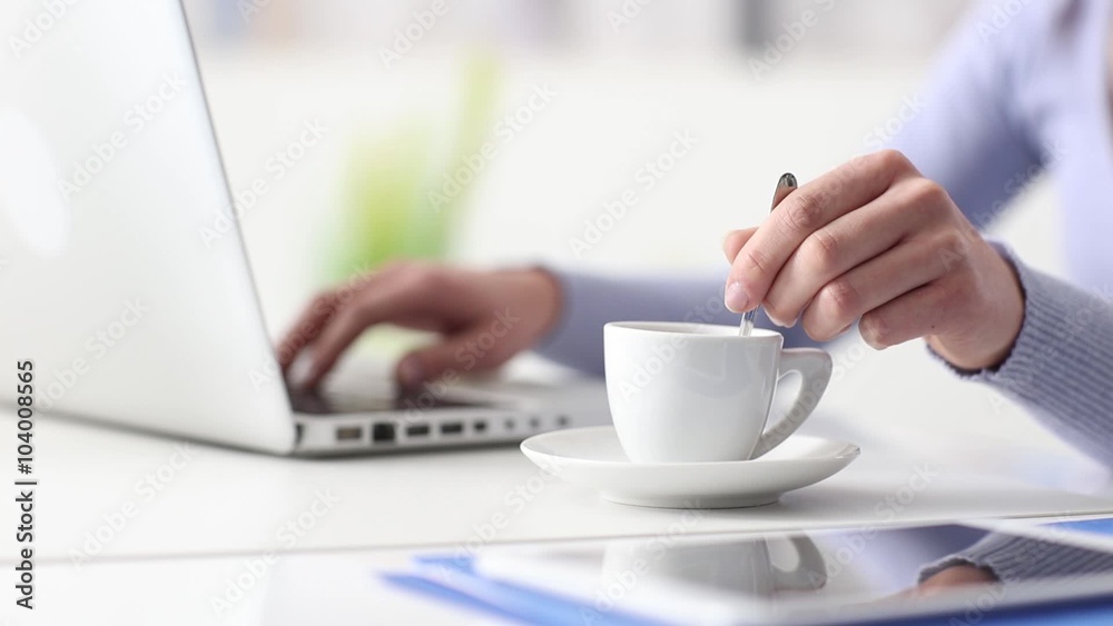 Young woman having a coffee break, she is stirring her espresso and using a laptop, hand close up, seamless loop