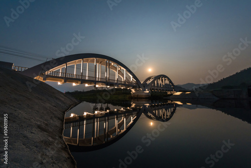 Old white railway bridge constructed against the moon in night a