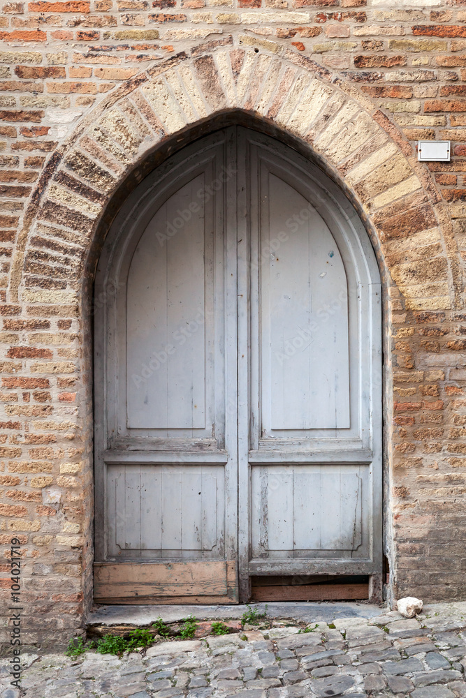 Old gray wooden door with arch in brick wall