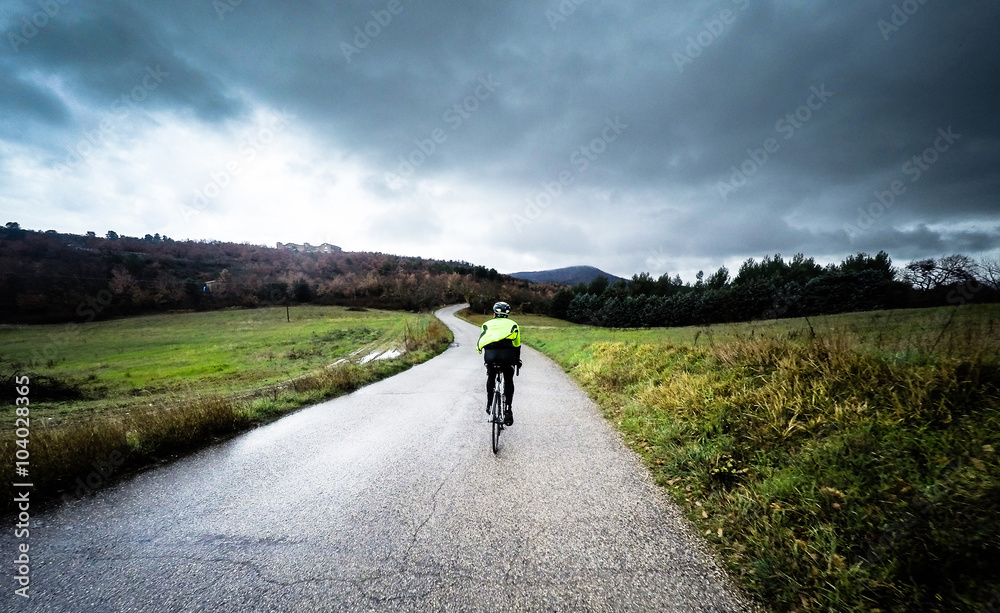 Obraz premium man on a bicycle ride along a mountain road during a storm