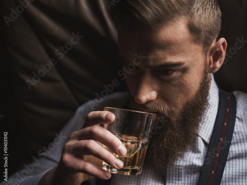 Cheerful bearded businessman is drinking expensive whisky